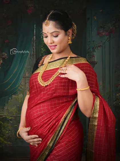 A beautiful studio portrait of a mother-to-be in a traditional red saree, adorned with gold jewelry.