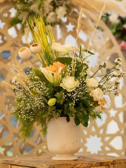Pastels are the new highlights. A beautiful floral arrangement with white roses and baby's breath in a simple white vase, set against a wooden jali backdrop, creates a look of understated elegance.
