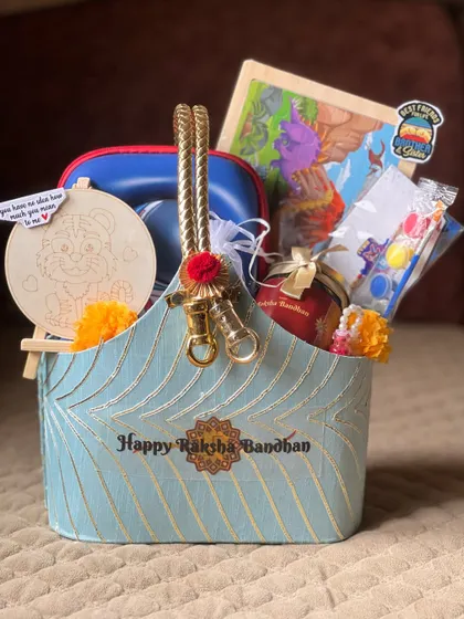 An elegant Raksha Bandhan hamper in a beautiful blue and gold basket. I've included a paintable craft, a puzzle, and other gifts suitable for both a brother and his family.