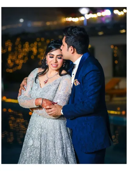 A tender moment with the groom kissing the bride's forehead. The warm glow of the background lights adds to the romantic and intimate feel of this outdoor reception shot.