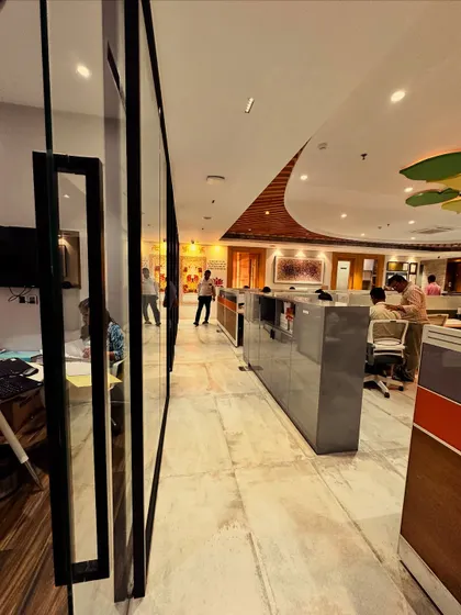 This angle captures the flow and movement within the office. The marble flooring and strategic lighting guide you through the space, leading past the private cabins and towards the collaborative work zones, all under the canopy of the symbolic tree.
