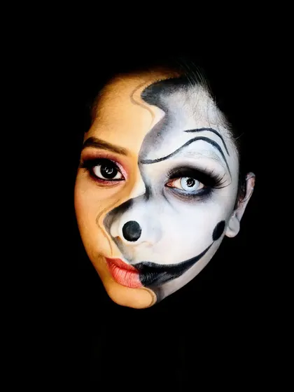A "two-faced" illusion makeup look, blending a beauty makeup side with a black-and-white clown character. This is an advanced technique that challenges students to think about light, shadow, and perspective.