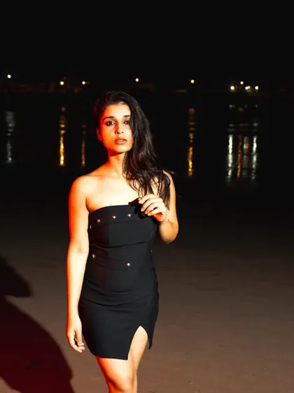 A night beach shoot using flash to illuminate the model against the dark sea. The distant city lights add a beautiful bokeh effect.