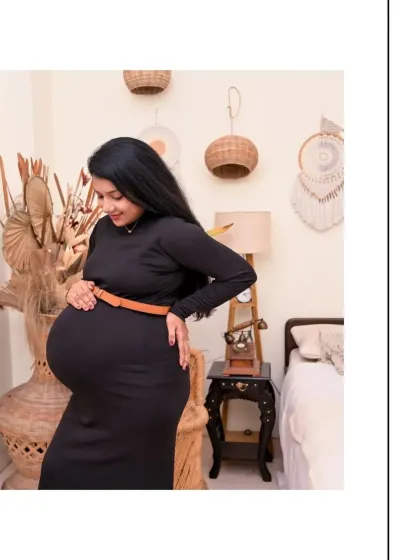 A side-profile portrait that beautifully showcases the pregnancy silhouette. The mom-to-be is wearing a simple black bodycon dress, and the warm, earthy tones of the Boho decor complement her look perfectly.