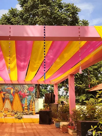 A wider angle of the outdoor Haldi venue, showing the pink and yellow fabric canopy that provides shade and color to the event.