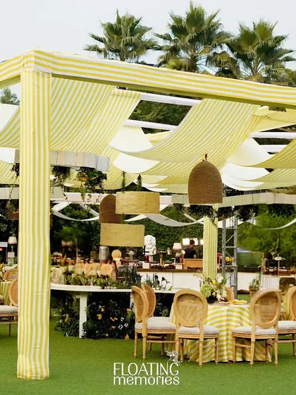 An expansive view of the 'What will you bee?' baby shower. The custom canopy with striped fabric, elegant seating arrangements, and lush greenery created a luxurious and cohesive outdoor setting.