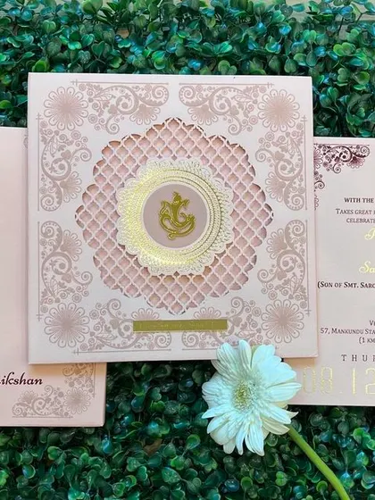 A beautiful pastel pink invitation with a laser-cut 'jaali' design and a central glass Ganesha logo. This card perfectly blends modern techniques with traditional symbols.