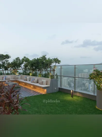 A view of the terrace lounge area at dusk, with the city lights beginning to twinkle in the background. The combination of soft lawn, comfortable seating, and perimeter trees creates a serene atmosphere.