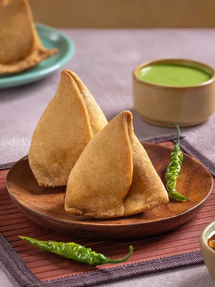 Two golden-brown samosas served with green and tamarind chutneys, a timeless Indian snack.