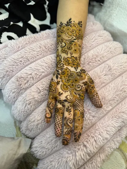 This intricate henna design features dense paisley and floral work, covering the entire back of the hand and wrist.