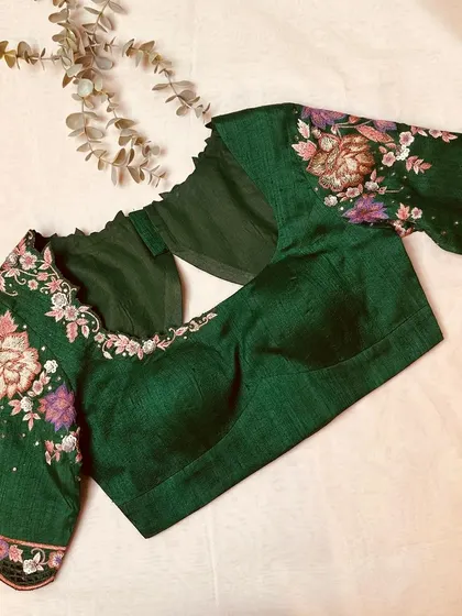 An emerald green blouse with stunning floral embroidery on the sleeves, showcasing craftsmanship at its best.