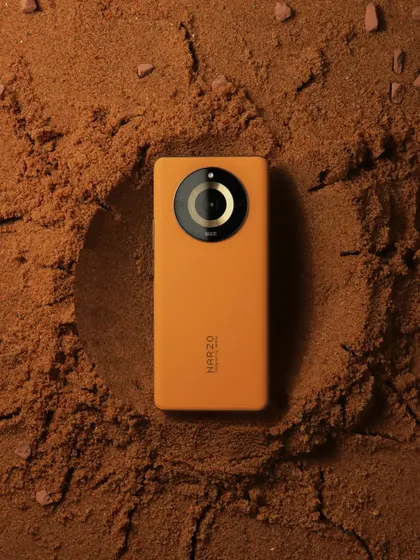 A top down shot of the orange realme Narzo phone placed in a crater of sand, continuing the "Mars terrain" theme.