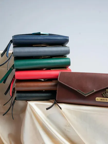 A stack of the Women's Nexa clutches showing the variety of colors available, with a personalized brown clutch in the foreground.