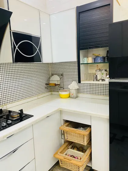 A compact kitchen corner featuring a rolling shutter for appliances and open wicker baskets for vegetables. The checkered backsplash adds a classic, retro feel.
