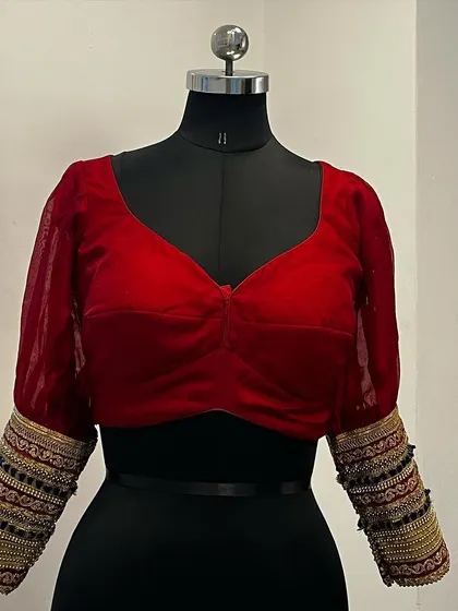 A beautiful red velvet blouse with sheer puff sleeves and heavily embellished cuffs.