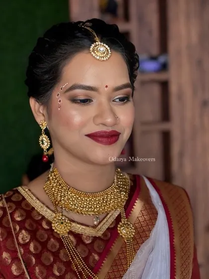 A soft glam beauty look for a wedding guest. This look features a classic red lip and subtle, traditional face painting (Kolka design) for an elegant touch.