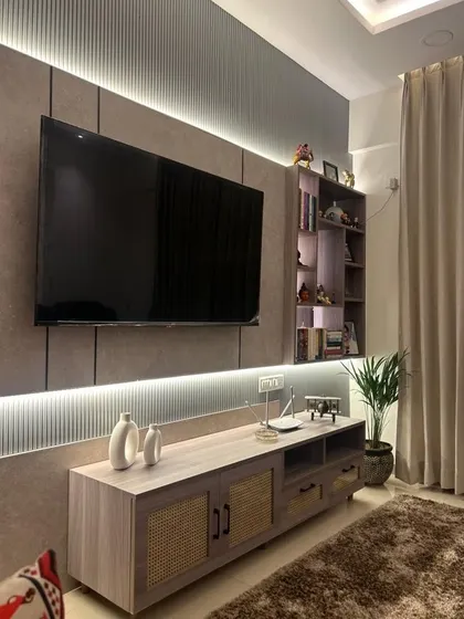 This TV unit design combines a soft beige finish with cane webbing on the cabinet doors, adding a touch of bohemian charm. The backlit panel and fluted details create a warm and inviting ambiance in the living room.