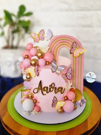 A dreamy butterfly and rainbow cake for a little one's birthday. The pastel pinks, gold details, and cascade of spheres make this a whimsical and magical celebration cake.