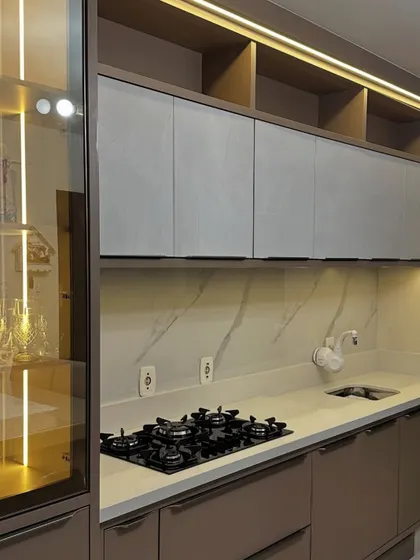 A sophisticated kitchen design featuring matte taupe cabinets and a marble-veined backsplash. The glass-fronted crockery unit with internal lighting adds a touch of class and display space.
