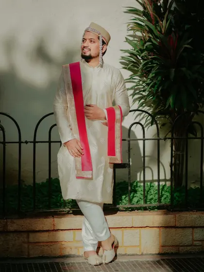 A portrait of the groom in a classic off white kurta, looking dapper and ready for his wedding day.