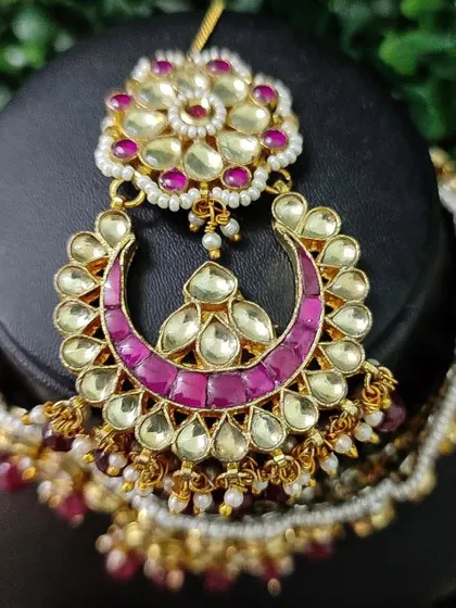 A close-up of a rental choker featuring a crescent moon design with kundan and magenta enamel work.