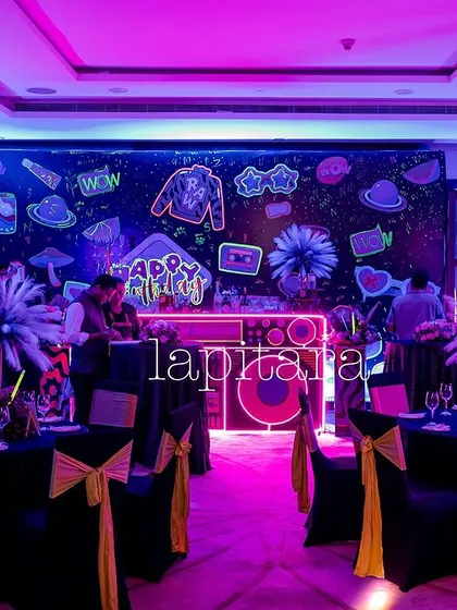 The dining area of the neon party, with tables set under the glow of purple blacklights and a wall covered in neon graffiti art.