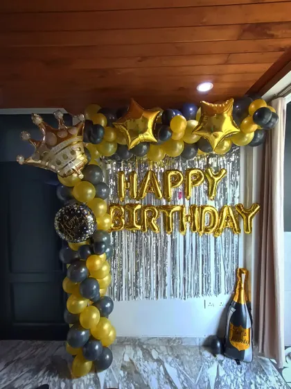 A black and gold themed birthday party with a balloon arch, foil letters, and props like a crown and champagne bottle.
