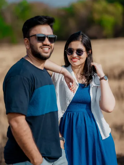 A cool, casual pre-wedding portrait of a couple in sunglasses, enjoying a sunny day in an open field.