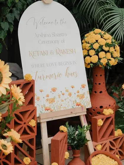 Welcome to the Haldi! We styled this entrance with rustic terracotta pots, cheerful sunflowers, and a custom welcome sign to set a warm and inviting tone for the "turmeric hues" celebration.