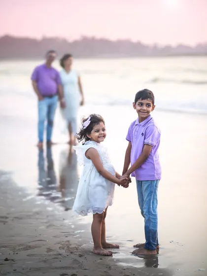 A sweet sibling portrait on the beach, with their parents watching lovingly in the background. This composition tells a beautiful story of family.