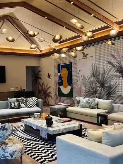 This recreational lounge in a corporate office is designed to feel like a high-end living room. With comfortable sofas, patterned armchairs, a striking black-and-white rug, and tropical-themed wallpaper, it's a space for employees to relax and connect.