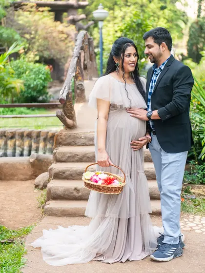 A lovely portrait on a rustic bridge. The expecting mother holds a basket of flowers, adding a touch of color and softness to this romantic outdoor maternity scene.
