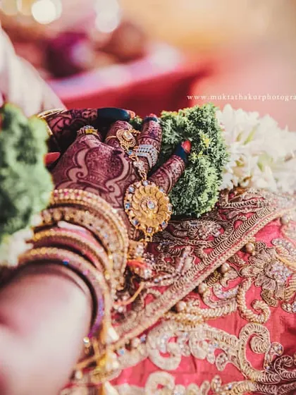A close-up of the bride's hands, showing her intricate henna design, bangles, and the garlands from the wedding ceremony.