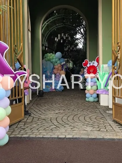 The entrance to an outdoor sea-themed party, with dolphin and crab character props on balloon columns guiding guests inside.