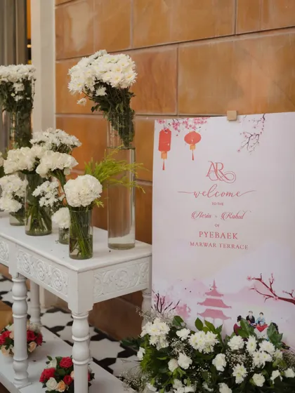 The welcome area for the Paebaek ceremony, featuring a sign with custom Korean-inspired artwork and elegant arrangements of white carnations.
