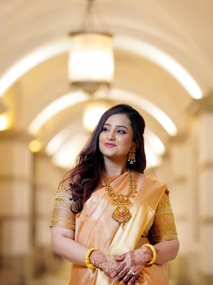 A stunning portrait of the bride in a golden silk saree. The soft lighting of the corridor and her thoughtful expression create an image of timeless elegance.