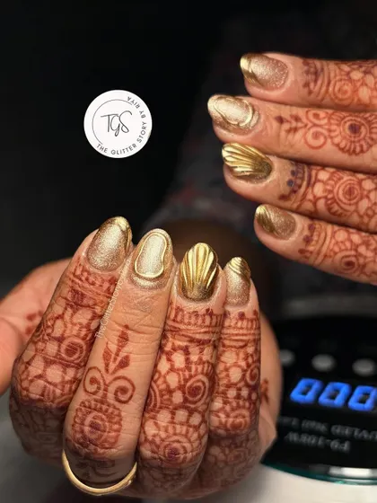 A bold, all-gold bridal look. These nails feature a solid gold chrome finish with a textured, 3D seashell-like design on the accent nail for a unique and glamorous style.