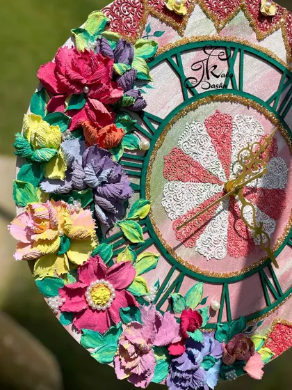 A close-up of a 16-inch clock with a pink-themed dial. You can see the detailed stenciling and the texture of the multi-colored flowers, each one carefully placed to create a balanced composition.