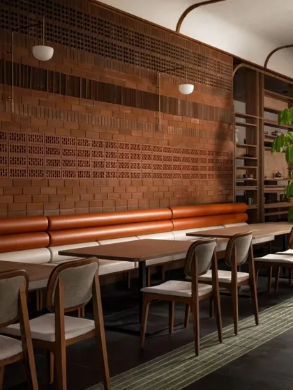 This seating area features a long, comfortable booth against a textured terracotta brick wall. The combination of warm leather-toned upholstery and natural wood chairs creates a cozy and inviting zone for guests to enjoy their meal.