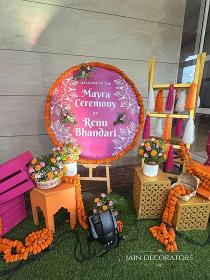 A personalized welcome for a Mayra ceremony. The custom sign is surrounded by bright marigolds, colorful tassels, and painted crates, creating a cheerful and inviting entrance for guests.