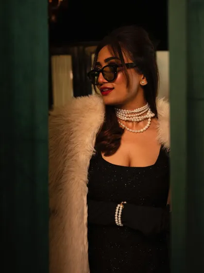 A final look at the 90s-inspired style. The combination of the voluminous hair, dark glasses, and pearl necklace creates a cohesive and stylish retro statement.
