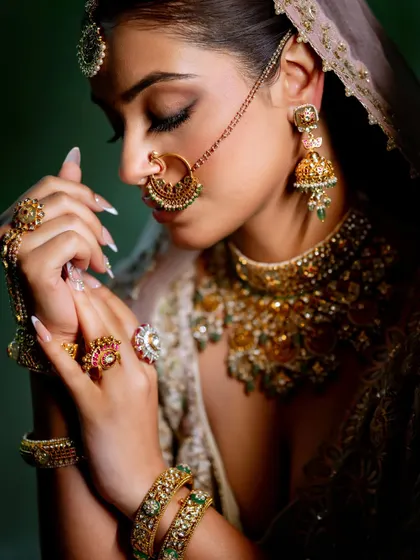 This shot highlights the intricate details of the jewelry and the soft, matte finish of the eye makeup. The bride's hands, adorned with henna and rings, add to the overall bridal beauty.