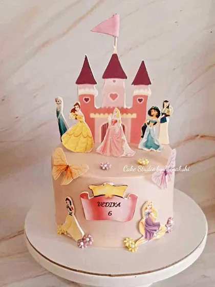 A Disney princess themed cake for a 6th birthday. This design features a castle topper and all of her favorite princesses, including Cinderella, Belle, and Jasmine.