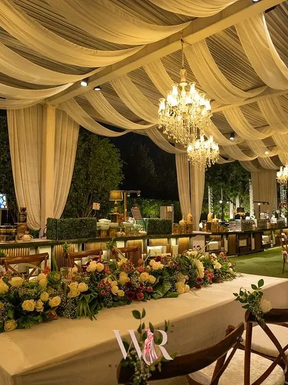 A view of the long head table, adorned with a lush floral runner. The setup is positioned to give diners a beautiful view of the entire reception space and the catering stations.