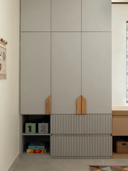 For a young collector of toys and books, I designed this bedroom with plenty of smart storage. The wardrobe features house-shaped handles and open cubbies at the bottom for easy access to their favorite things.