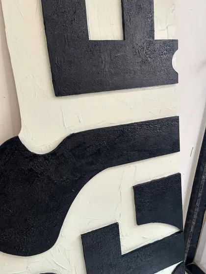 A close-up of the texture on the large black and cream abstract piece. The black sections have a rough, sandy texture that contrasts with the smoother cream background.