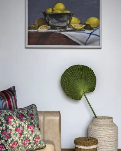 A detail shot of the guest room, where a lush green palm leaf and woven decor add natural texture, contrasting beautifully with the classical art and floral cushion.