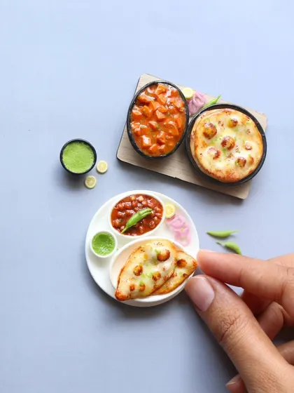Two versions of a naan and curry miniature, one on a plate and one on a wooden board.
