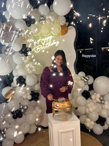 A sparkling celebration moment. The birthday girl cuts her cake in front of a chic white and black balloon backdrop, with sparklers adding to the festive magic.