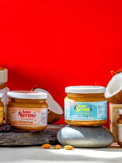 A bold product lineup of Being Better's various nut butters against a vibrant red background. This colorful shot showcases the entire range, with fresh ingredients like coconut and banana hinting at the different flavors.